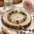 Green phantom quartz crystal bracelet with ruby charm and gold leaf pendant on wooden tray with lavender, Crystalvana