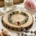 Green phantom quartz crystal bracelet with ruby charm and gold leaf pendant on wooden tray with lavender, Crystalvana