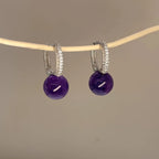 Hand holding natural amethyst S925 silver earrings fingers close-up, Crystalvana