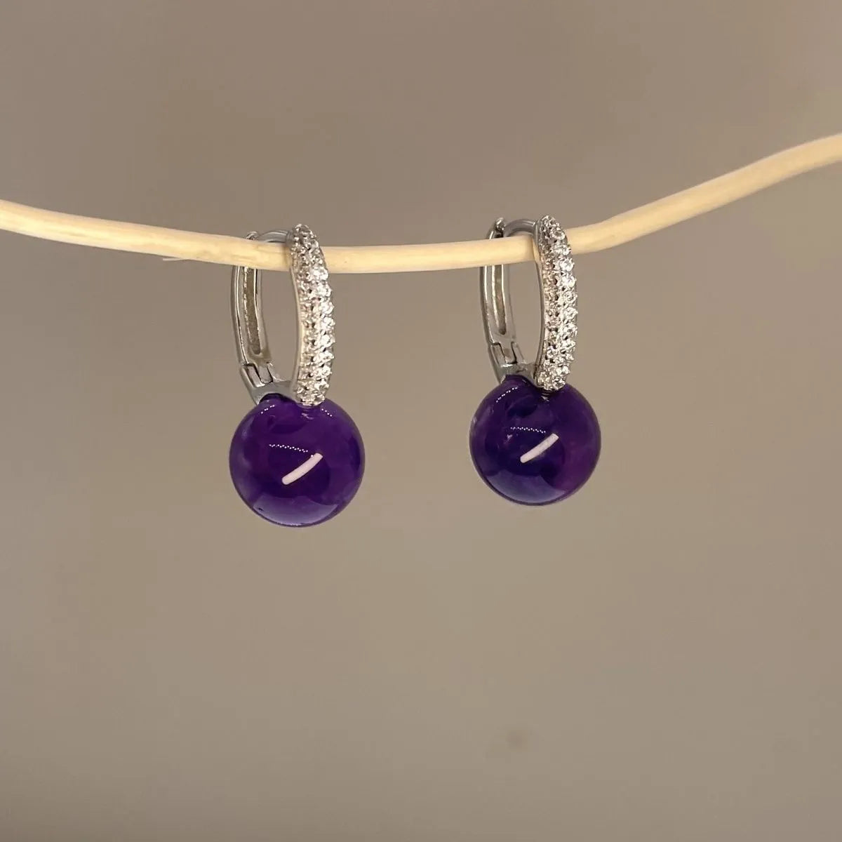 Hand holding natural amethyst S925 silver earrings fingers close-up, Crystalvana