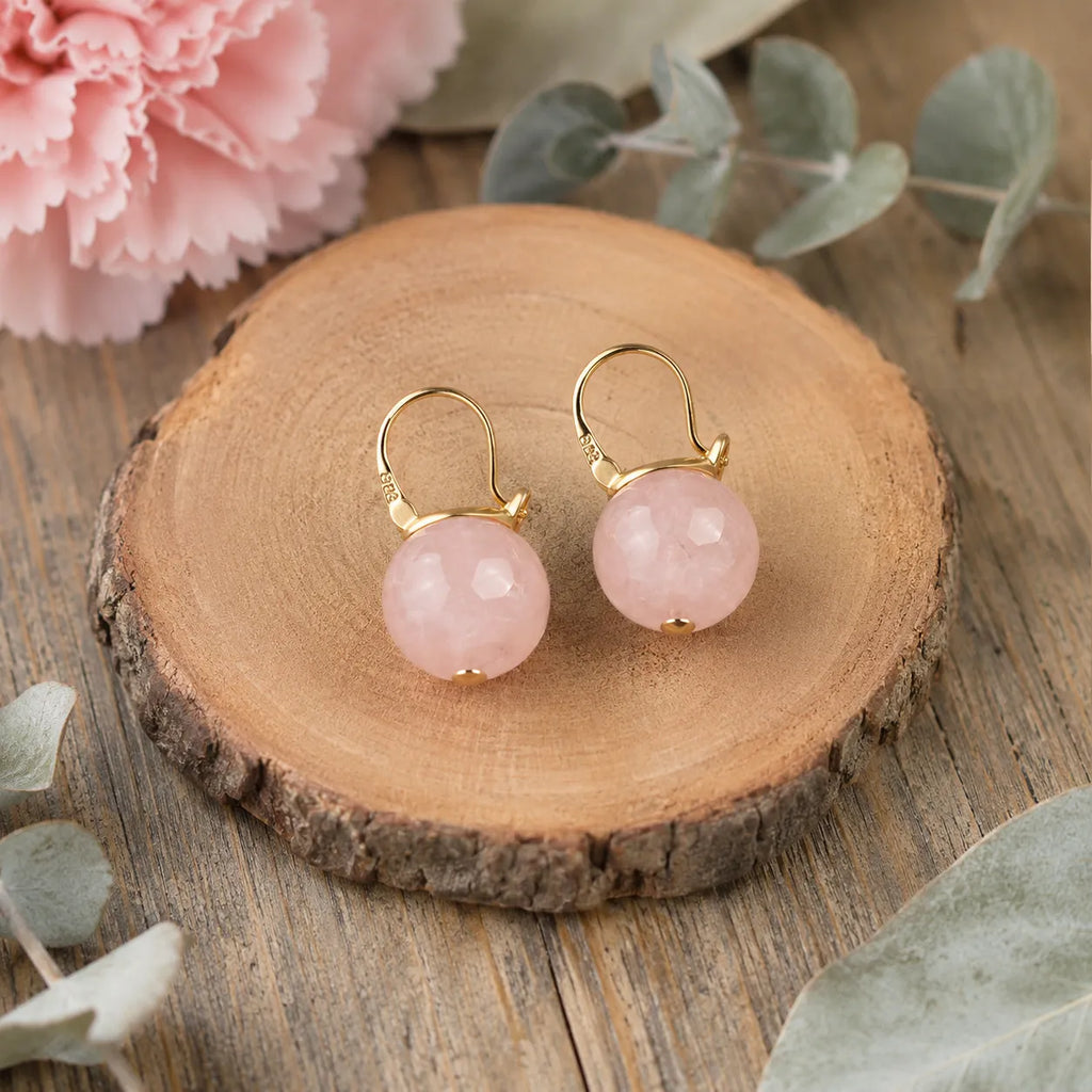 Natural rose quartz S925 silver buckle earrings flat lay on wood with eucalyptus and pink carnation, Crystalvana